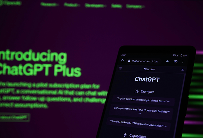 A phone with "ChatGPT" on the screen in front of a computer with "Introducing ChatGPT Plus" on the screen