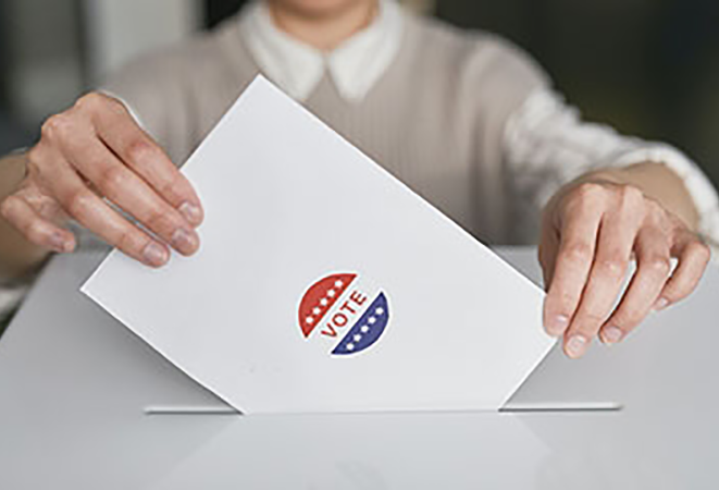 A person drops a voting ballot in a box