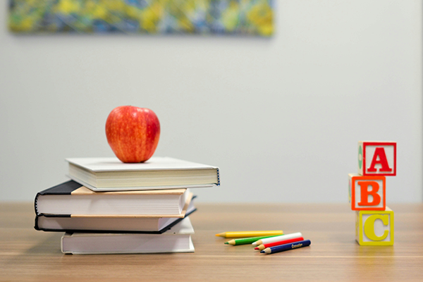 An apple on top of a stack of books, colored pencils, and a stack of letter blocks sitting on a table