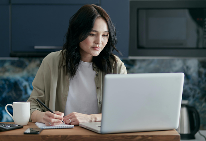 a person writes in a notebook while looking at a laptop