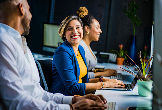 Three people smiling sitting in front of laptops