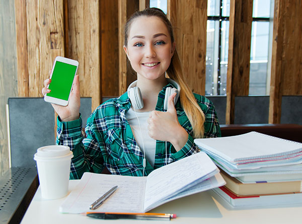 Student with books holding smart phone and giving thumbs up