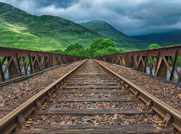 Train tracks leading into a horizon of verdant hills lightly shrouded by clouds