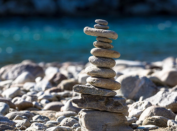 A small tower of stones balanced on top of each other on a stony beach with out-of-focus blue water in the background 