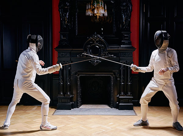 Fencers face-off in front of a fireplace 