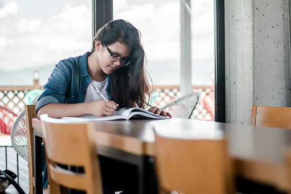 A person sitting at a table writes in a notebook