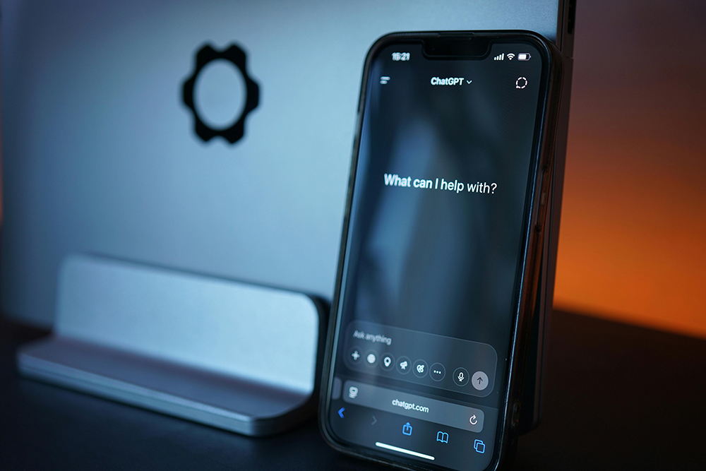 a phone screen displays the ChatGPT website, which says "What can I help with?"