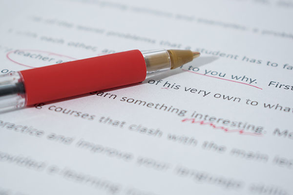 Close-up of red pen on top of a typewritten page with red editorial markings