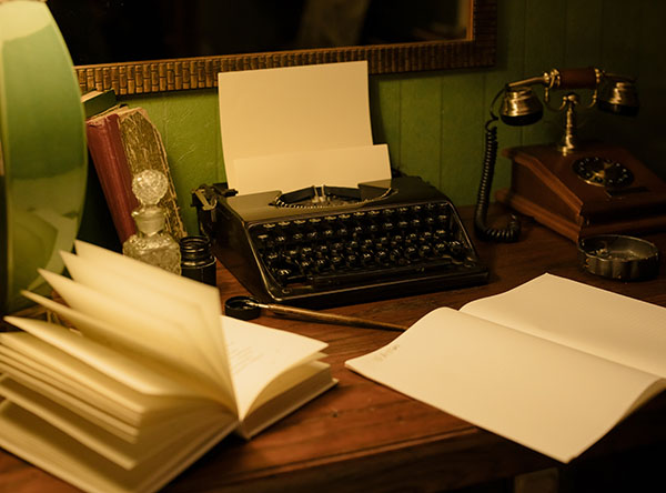 Typewriter and open notebooks on top of a desk next to an old-fashioned telephone